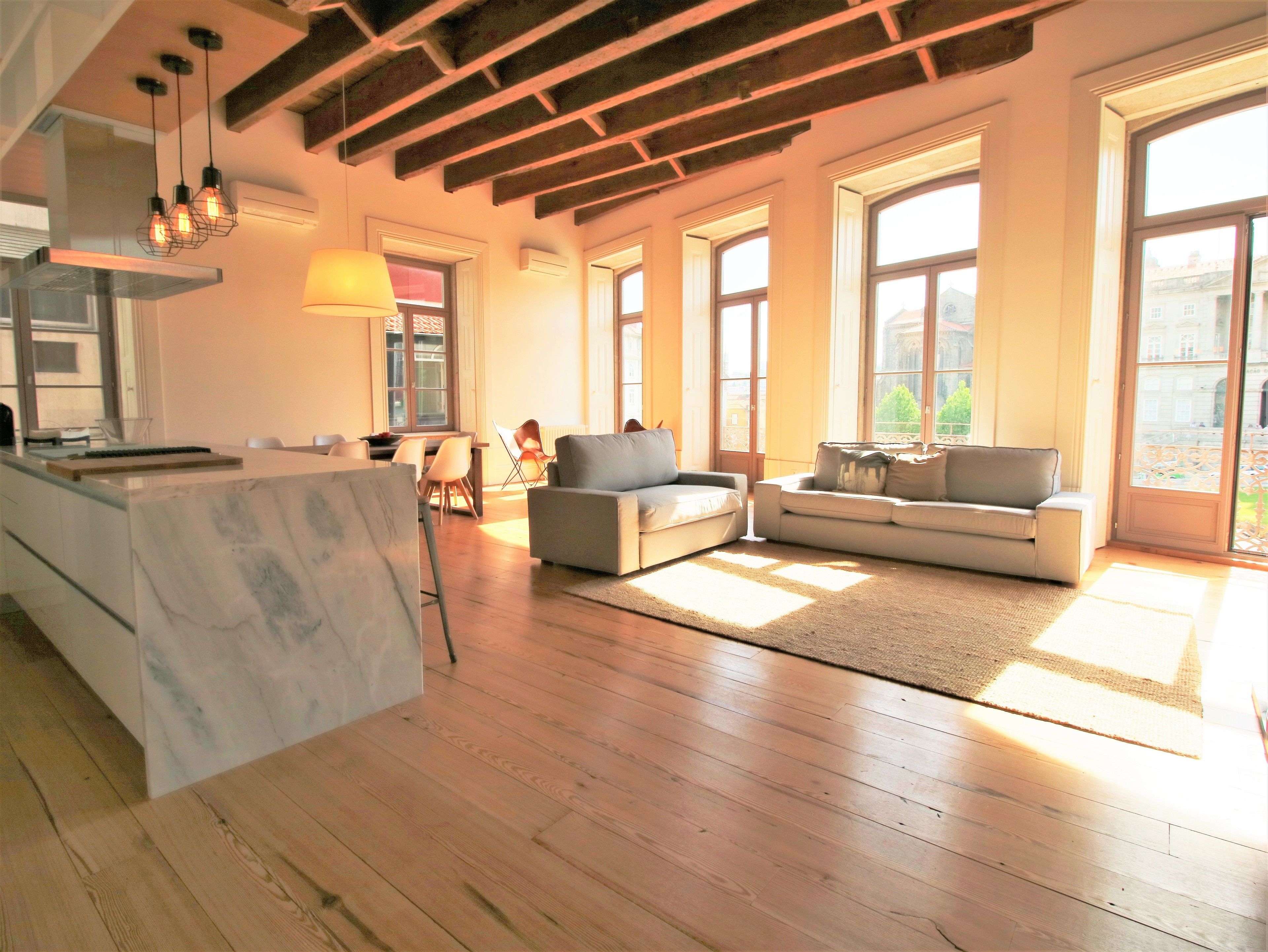 A spacious living area with a marble kitchen island, wooden flooring, and large windows offering views of the outside.
