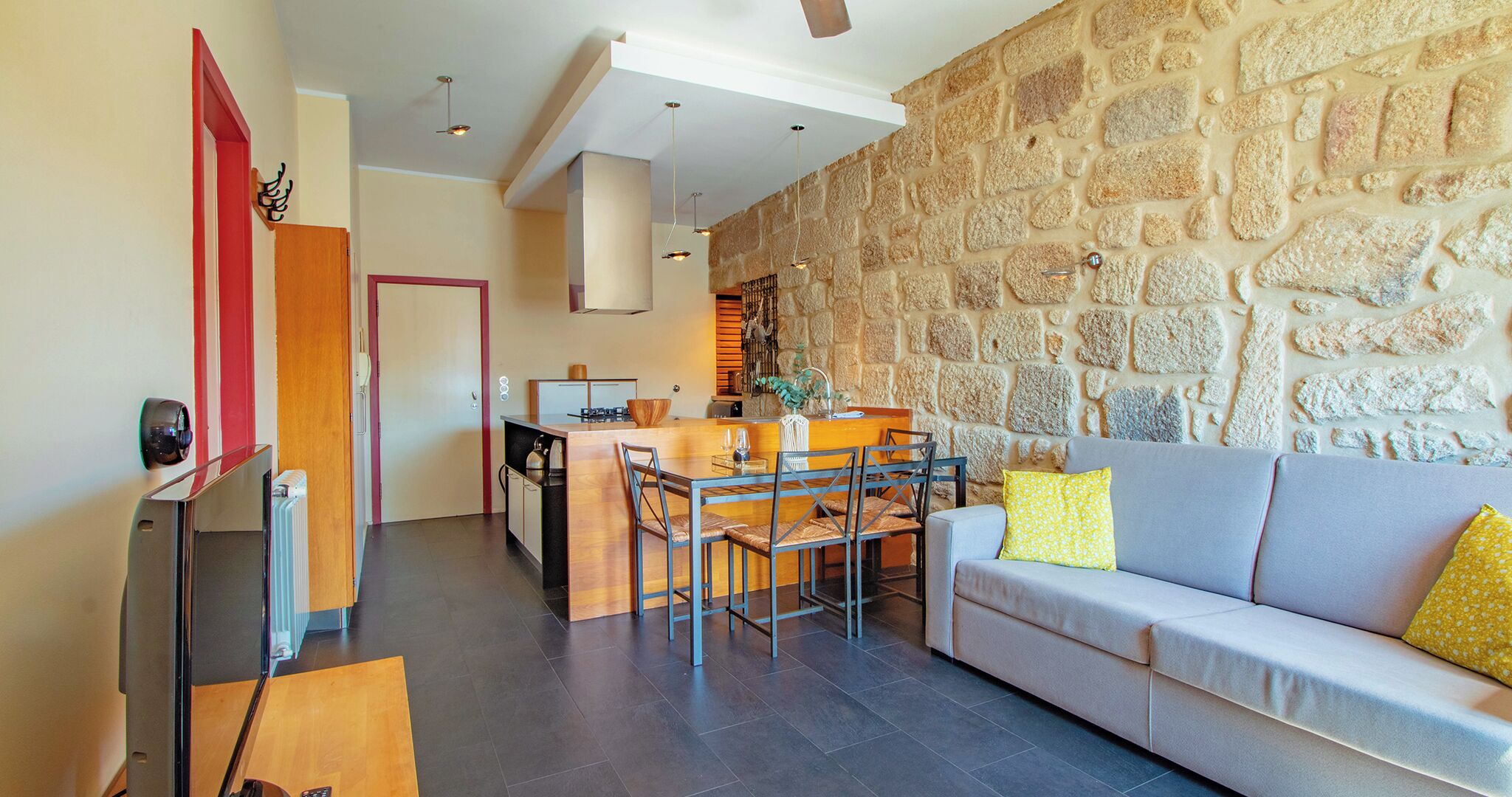 Una sala de estar moderna con una pared de piedra, un sofá gris y una mesa de comedor de madera con sillas.