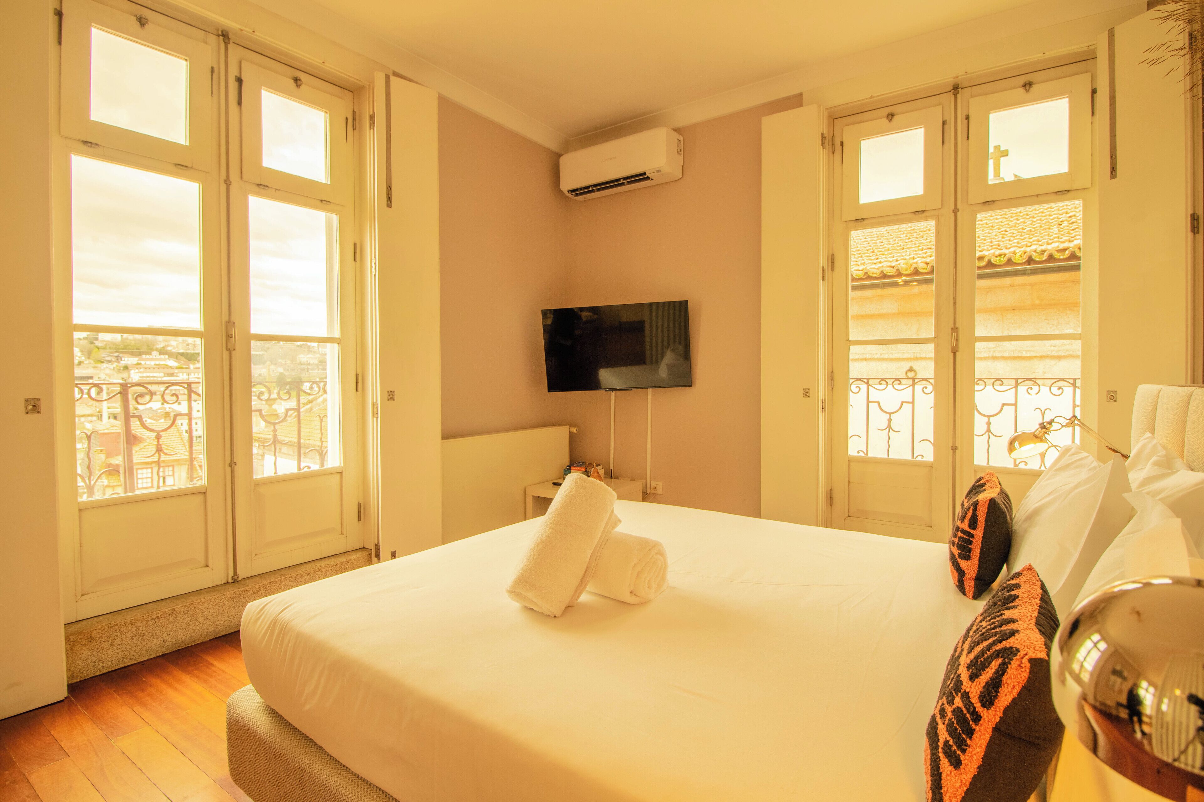 A hotel room with a bed, a flat-screen TV, and large windows with a balcony view.