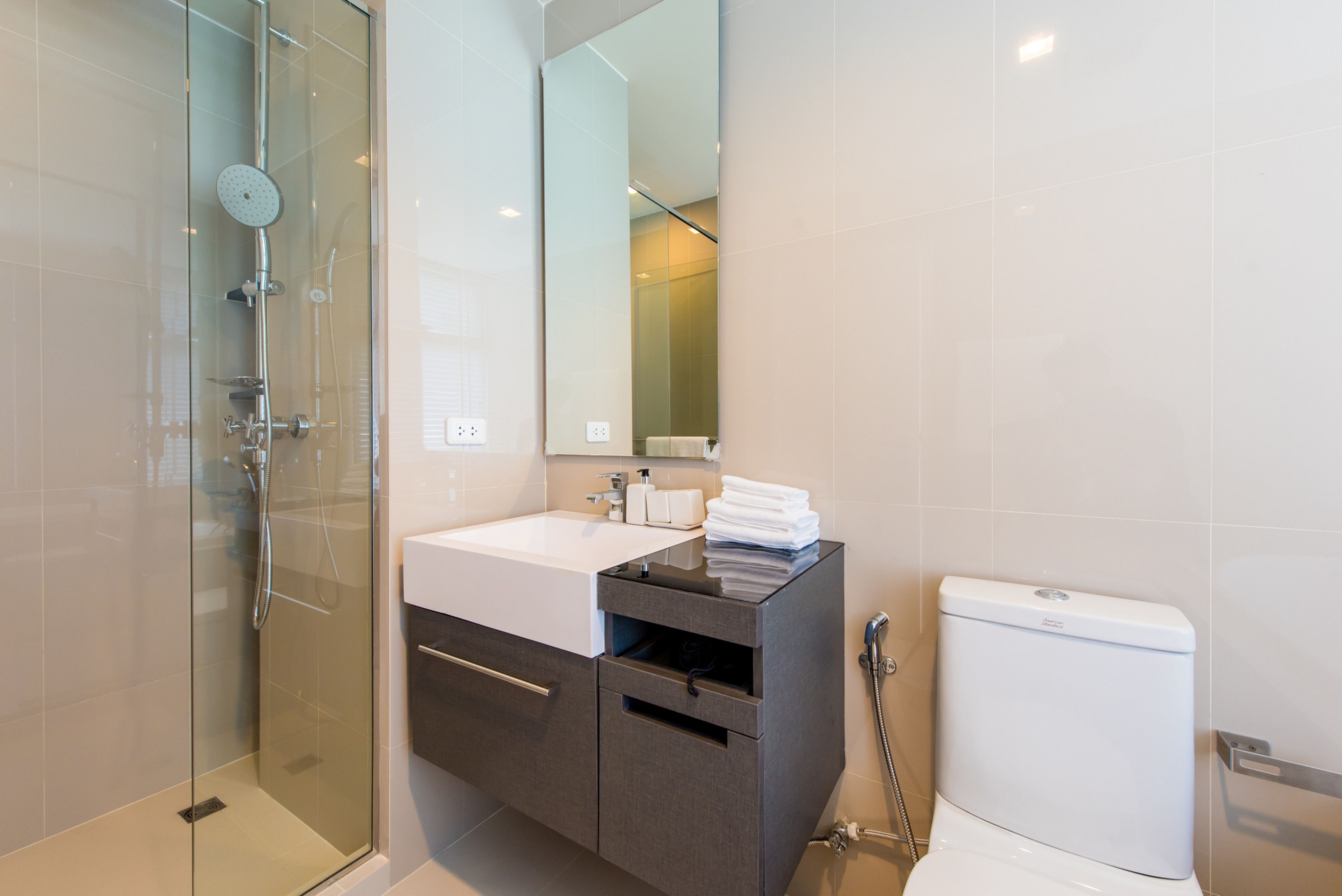 Un baño moderno con cabina de ducha de vidrio, un lavabo blanco y un mueble de tocador de tonos oscuros.