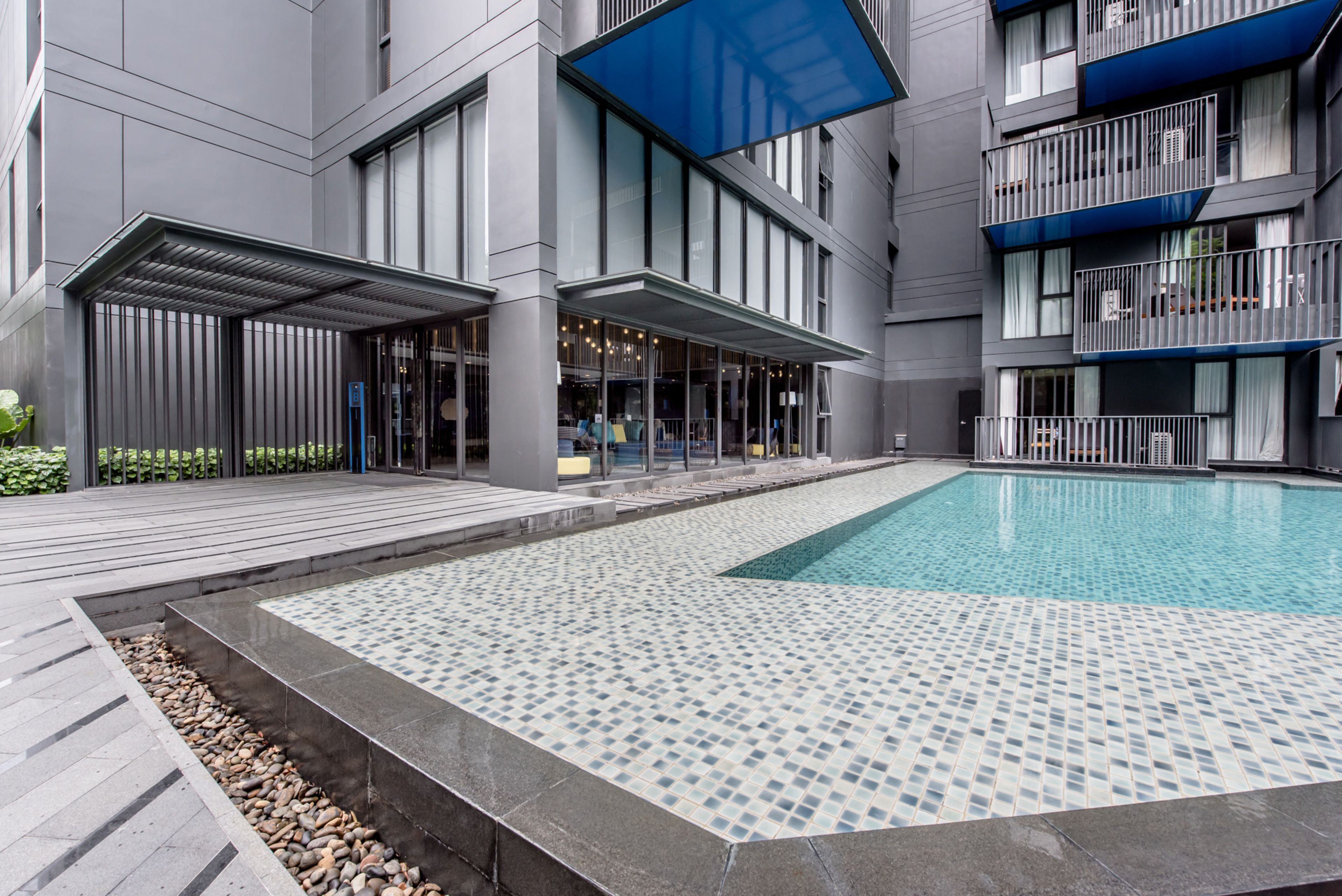 A modern building with a swimming pool, covered outdoor seating area, and a balcony with railings.