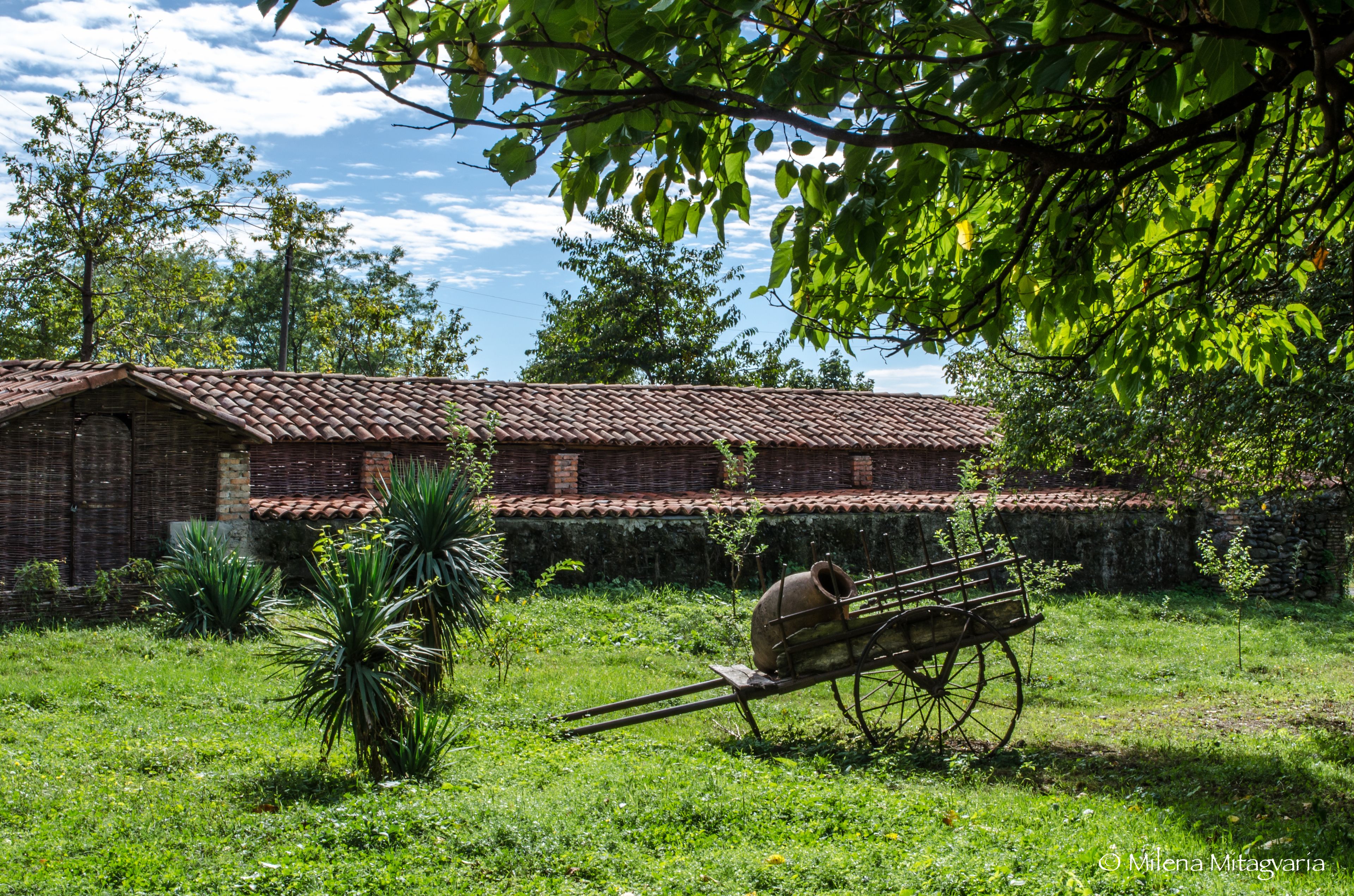 A rustic building with a tiled roof and a wheelbarrow in the foreground.