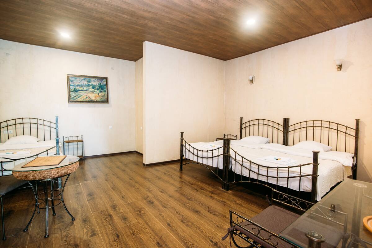 Una habitación con dos camas de estructura metálica, una mesita con un taburete tejido y un cuadro en la pared.