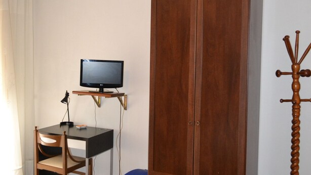 A room with a wooden wardrobe, a desk with a computer, a television, and a coat rack. - Albergo Abruzzese (Riano)