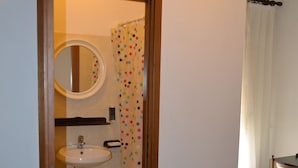 A bathroom with a wooden door, a sink, a mirror, and a shower curtain with a polka dot pattern. - Albergo Abruzzese (Riano)