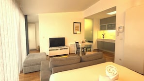 A modern hotel room with a sofa, a TV, a small dining table, and a kitchenette.