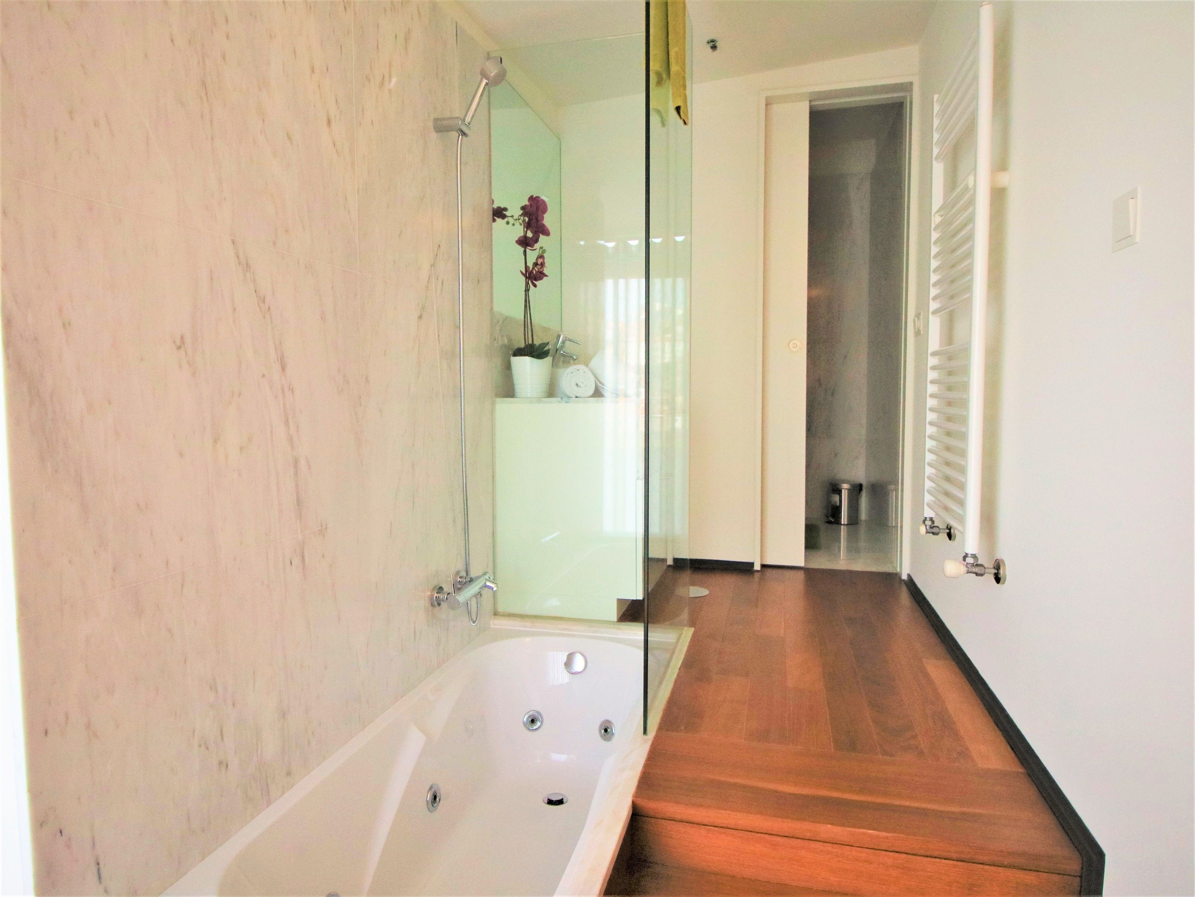Un baño con bañera, cabina de ducha de vidrio, piso de madera y puerta blanca.