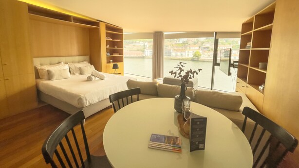 A modern hotel room with a large bed, a dining table, and a view of a river. - LUXURY VIEWS by YoursPorto (Vila Nova de Gaia)