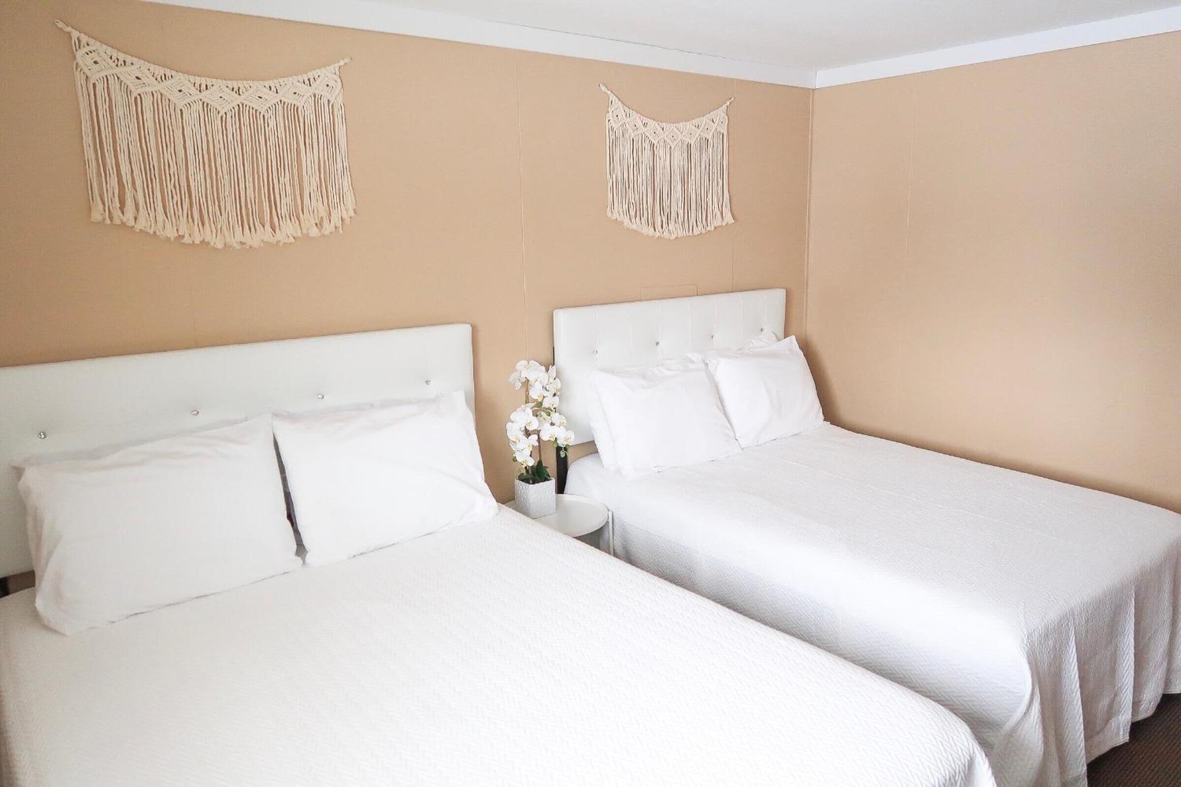 A hotel room with two beds, beige walls, and macramé wall hangings.