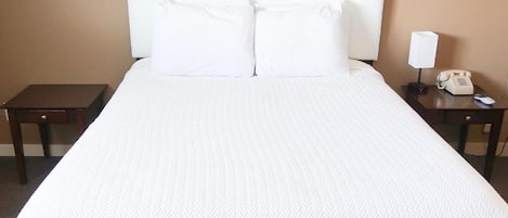 A hotel room with a large bed, a framed picture on the wall, a bedside table with a lamp, and a phone.