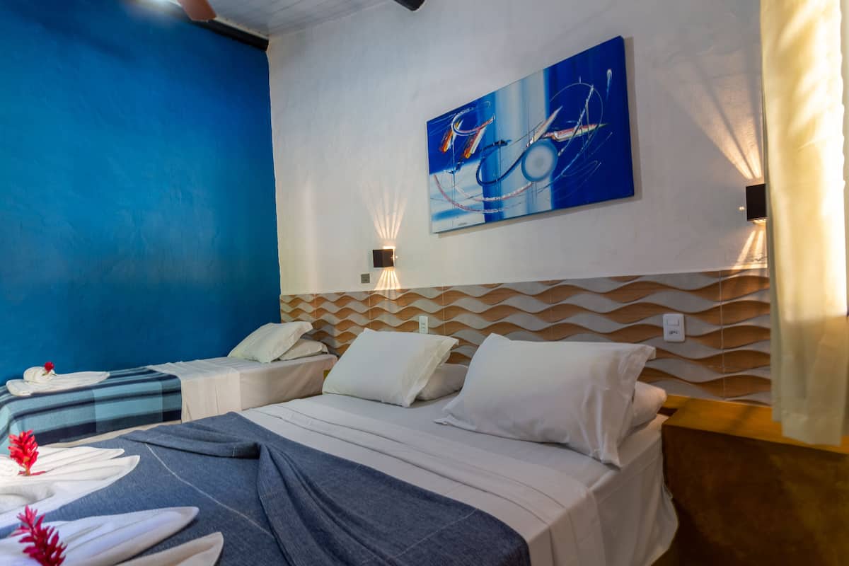 A hotel room with two beds, a blue accent wall, a modern abstract painting, and a wooden headboard.