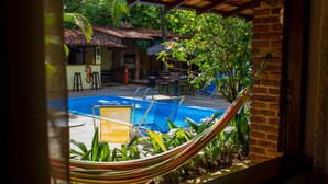 Un área de piscina con una hamaca, sillas y un edificio de ladrillo al fondo.