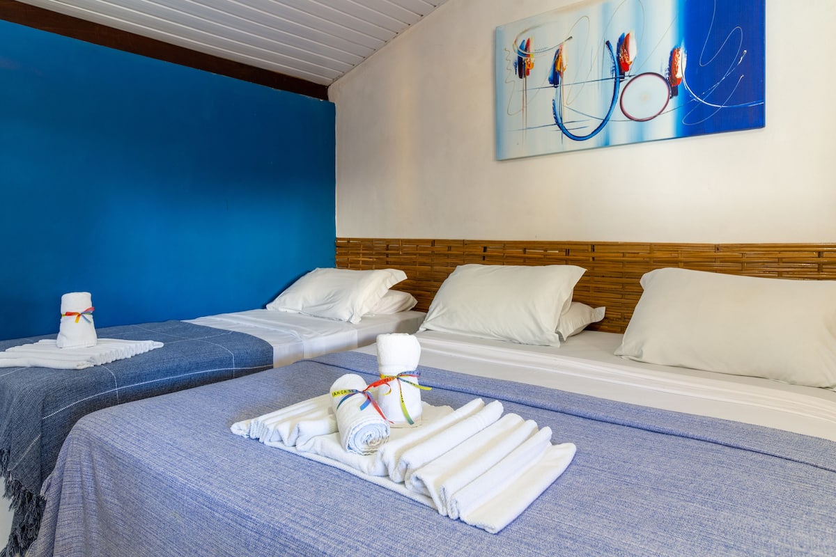 A hotel room with two beds, each with white linens and towels, a blue wall, and a wooden headboard.