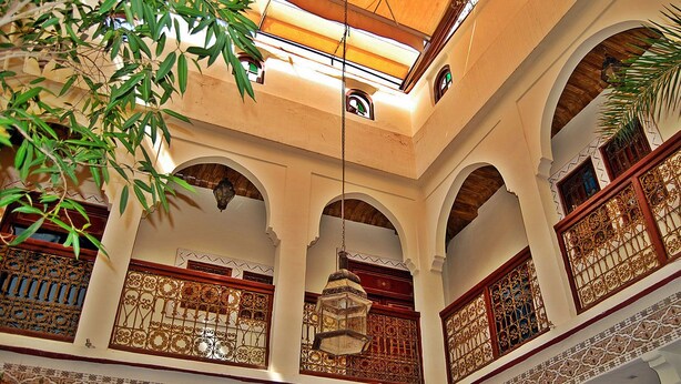 An interior with arched balconies, ornate metal railings, and hanging lanterns. - Riad Amiris (Marrakech)
