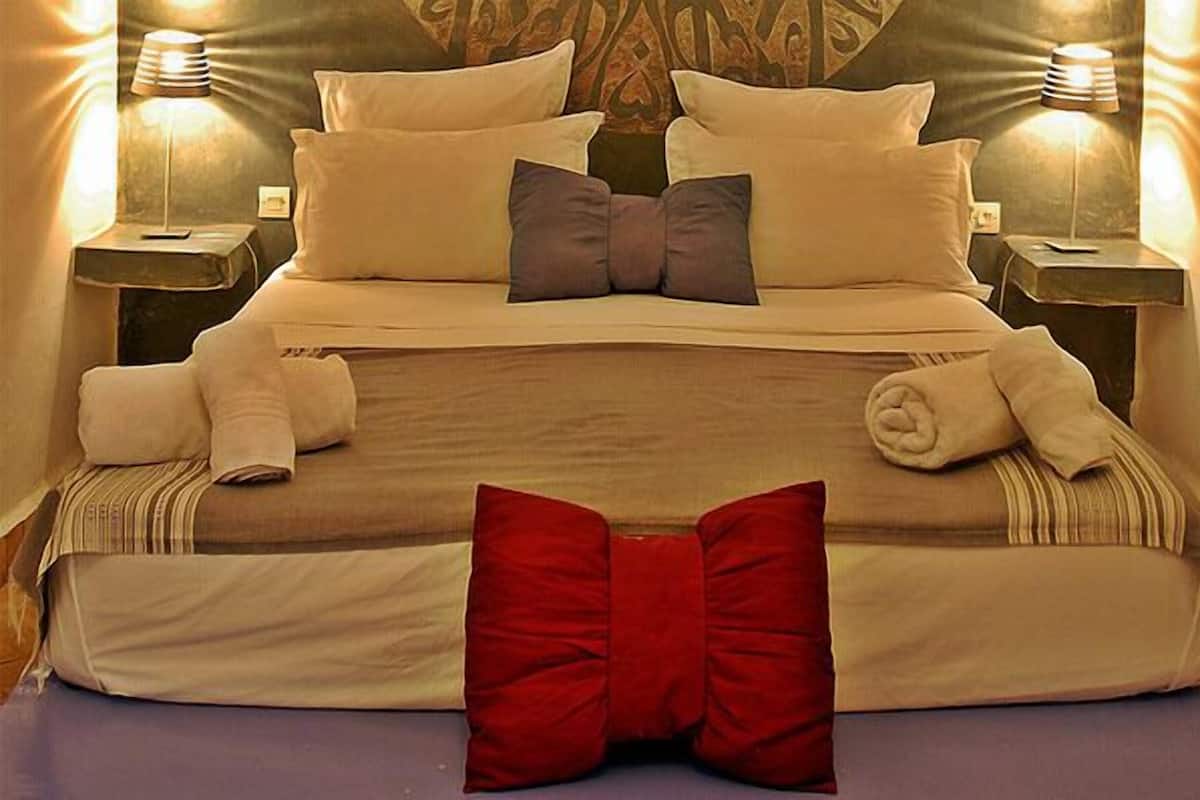 A neatly made bed with pillows and a red accent pillow, two bedside lamps, and a patterned headboard.