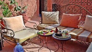 An outdoor seating area with metal chairs and cushions, a small round table with a tray of food and drinks, and a decorative lantern. - Riad Amiris (Marrakech)