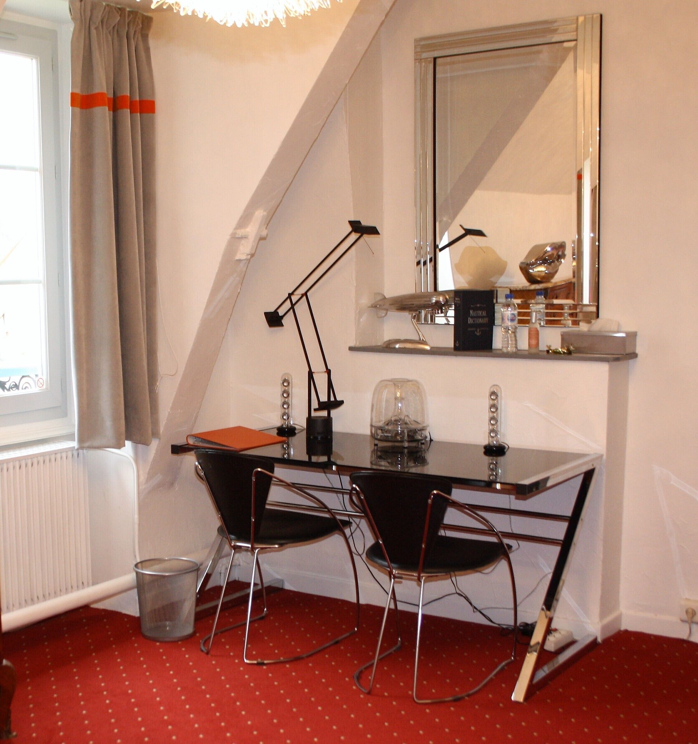 A small, modern room with a desk, two chairs, a mirror, and a radiator.