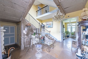 Um hall espaçoso com uma escadaria imponente, um candelabro e diversos objetos decorativos.