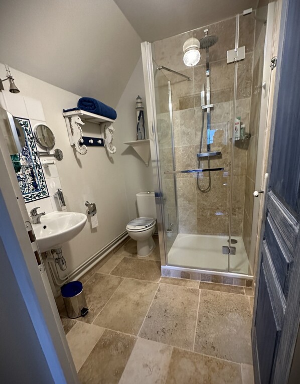 A bathroom with a glass-enclosed shower, a white sink, a toilet, and a blue towel rack.