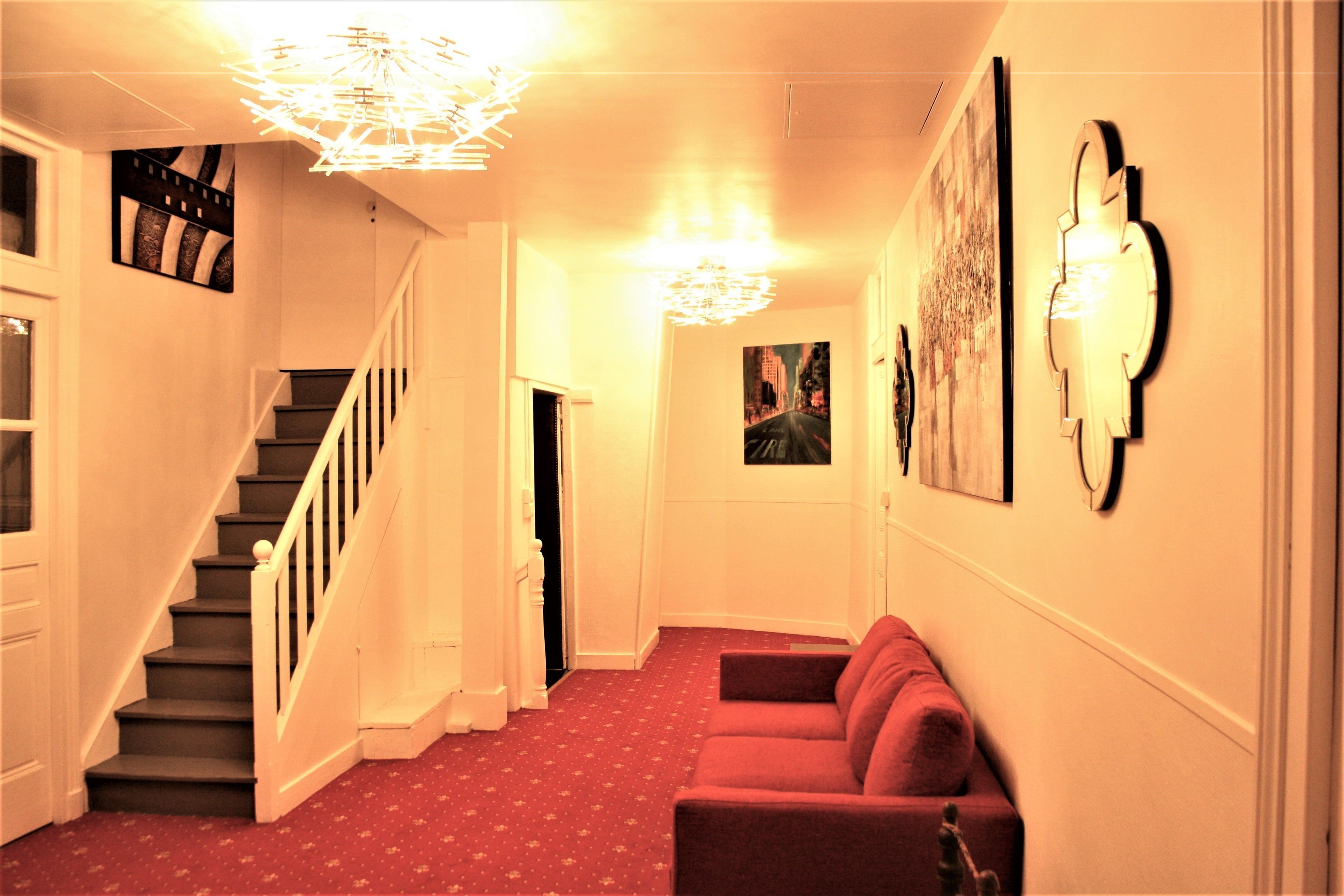 A hallway with a staircase, a red carpet, a red sofa, and wall art.