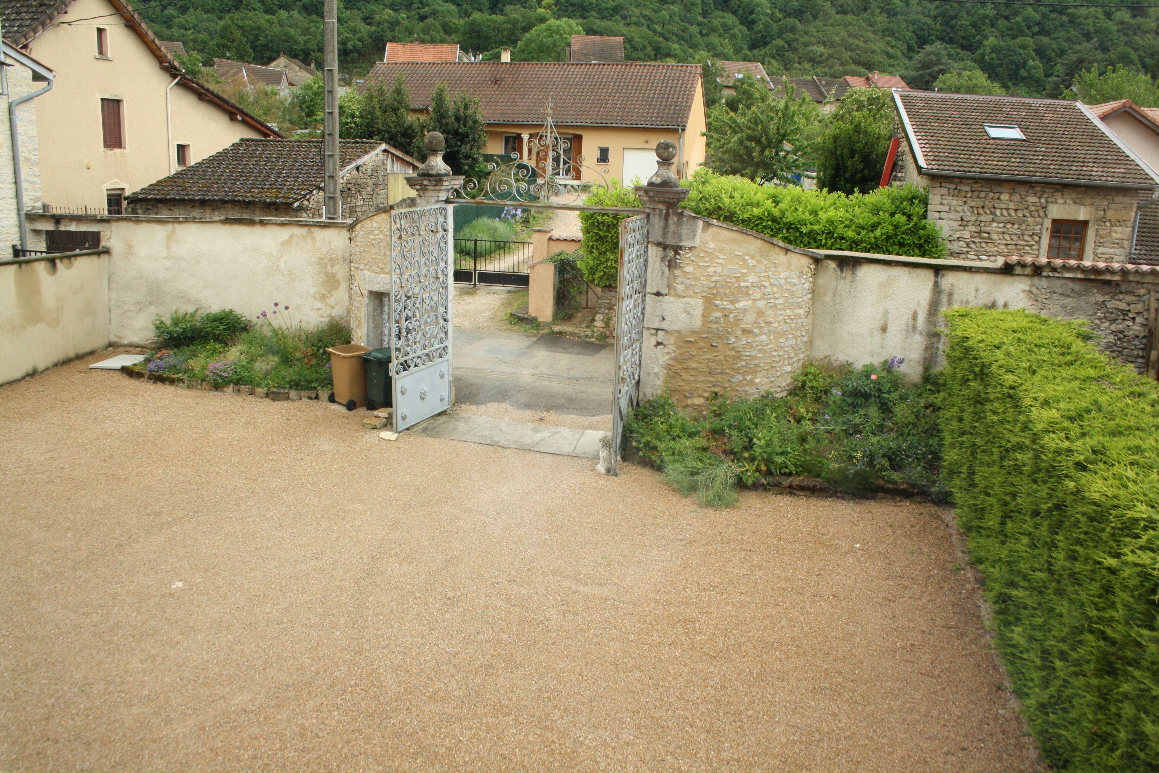 A rural village with stone houses, a gravel driveway, and a metal gate.