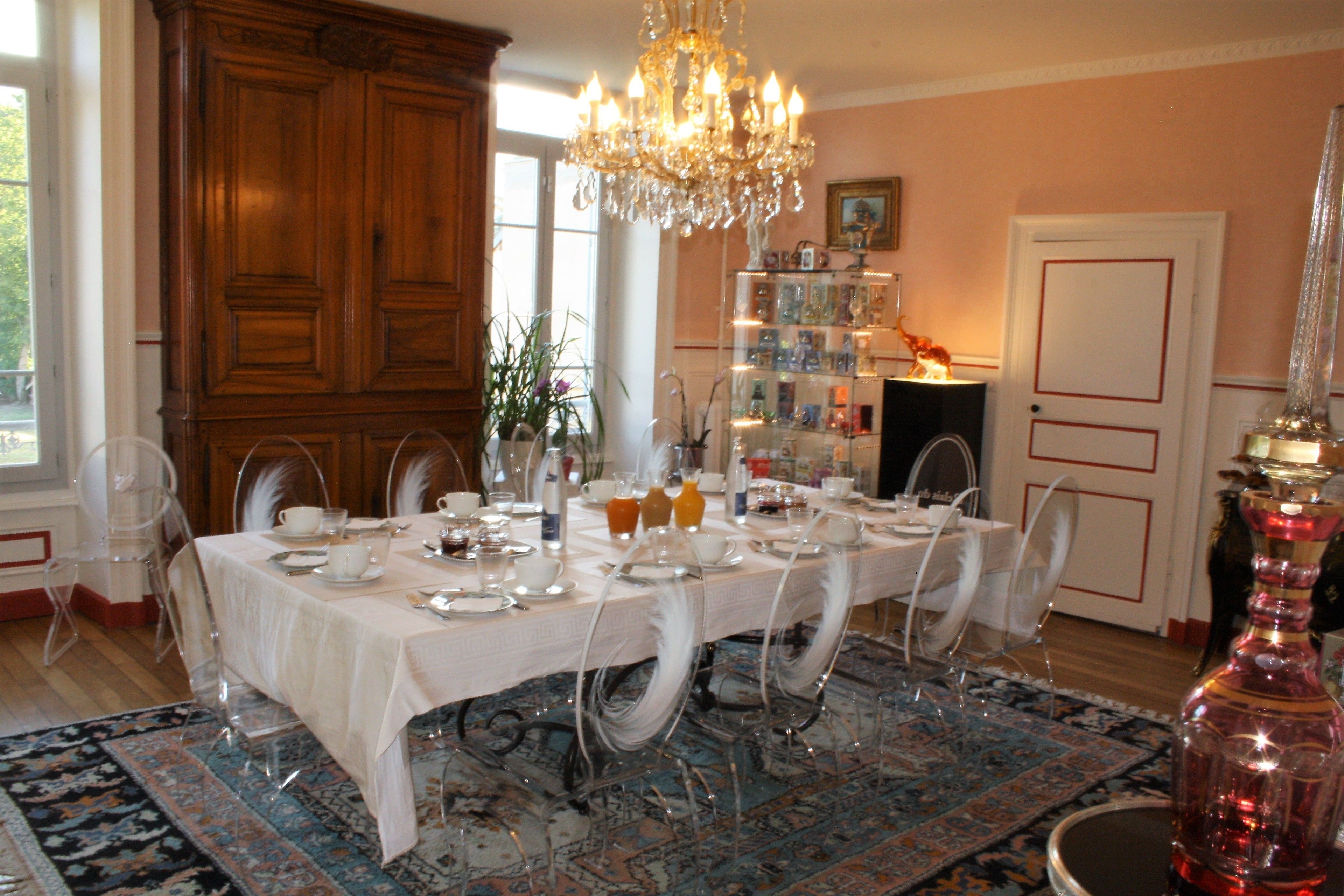 A dining room with a long table set for a meal, clear chairs, a chandelier, and a large wooden cabinet.