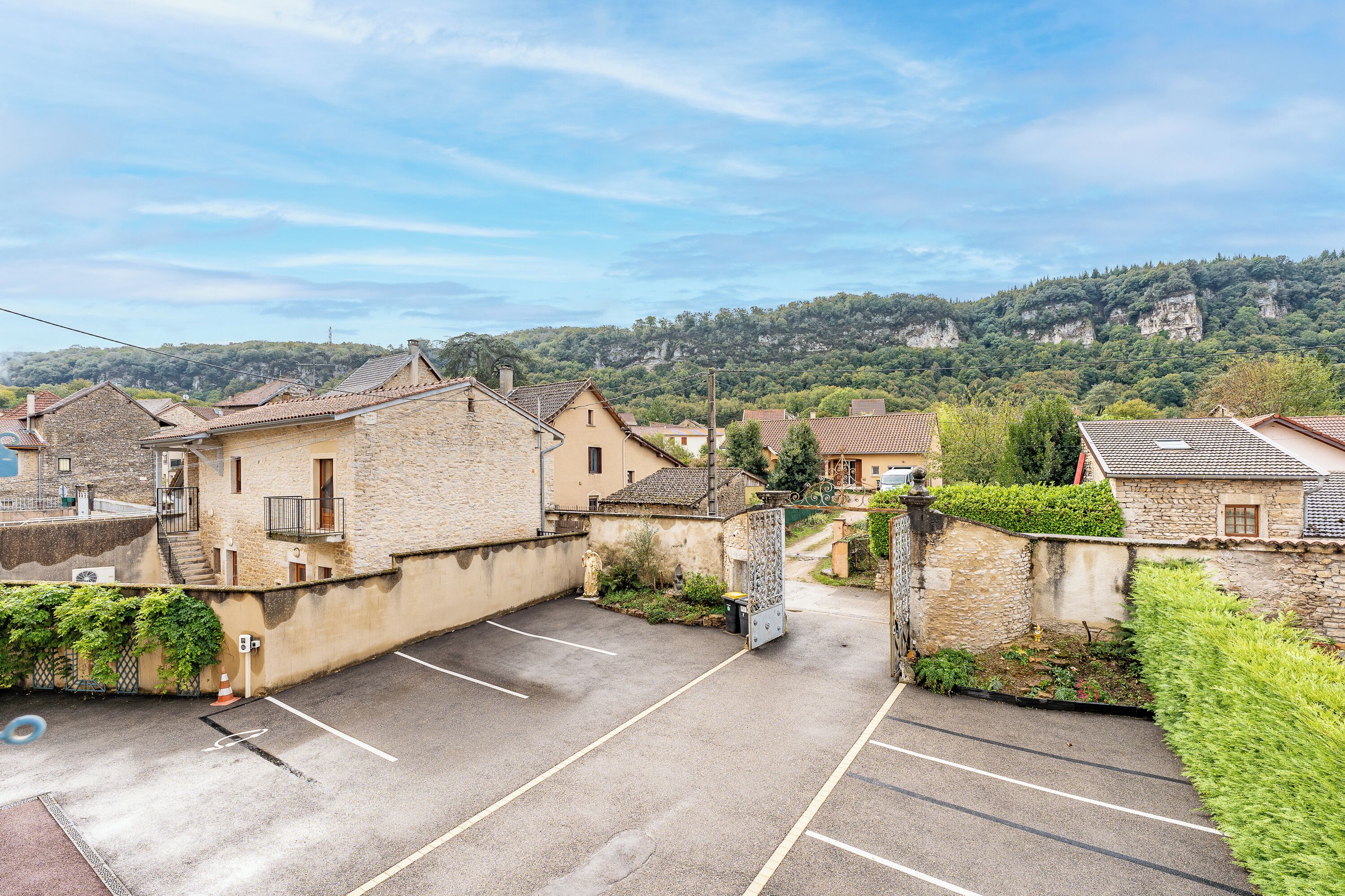 A parking area with stone buildings, a clear sky, and a hilly landscape in the background.