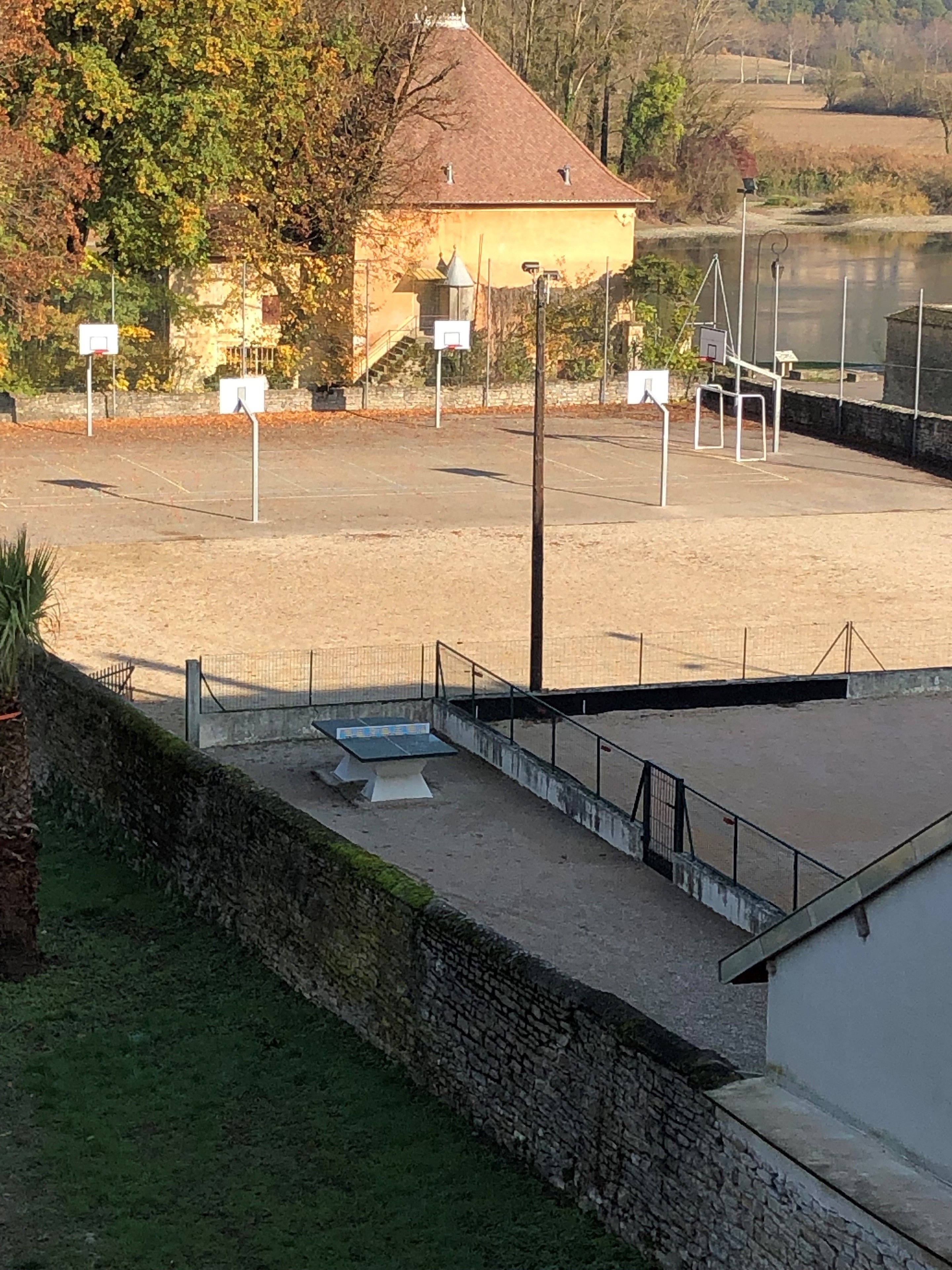 A basketball court with multiple hoops, a stone wall, and a building in the background.