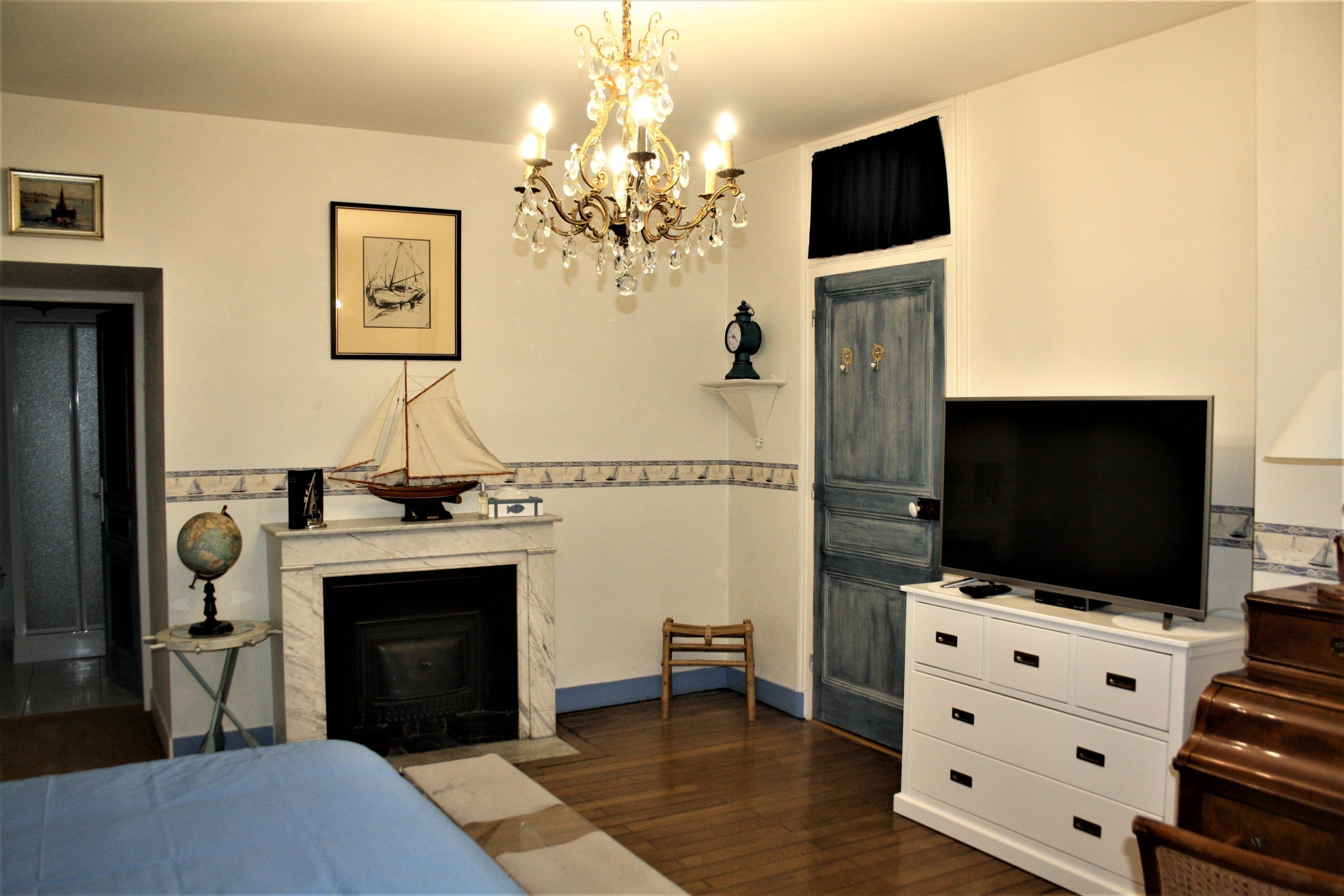 A bedroom with a bed, a television, a fireplace, a globe, and a chandelier.