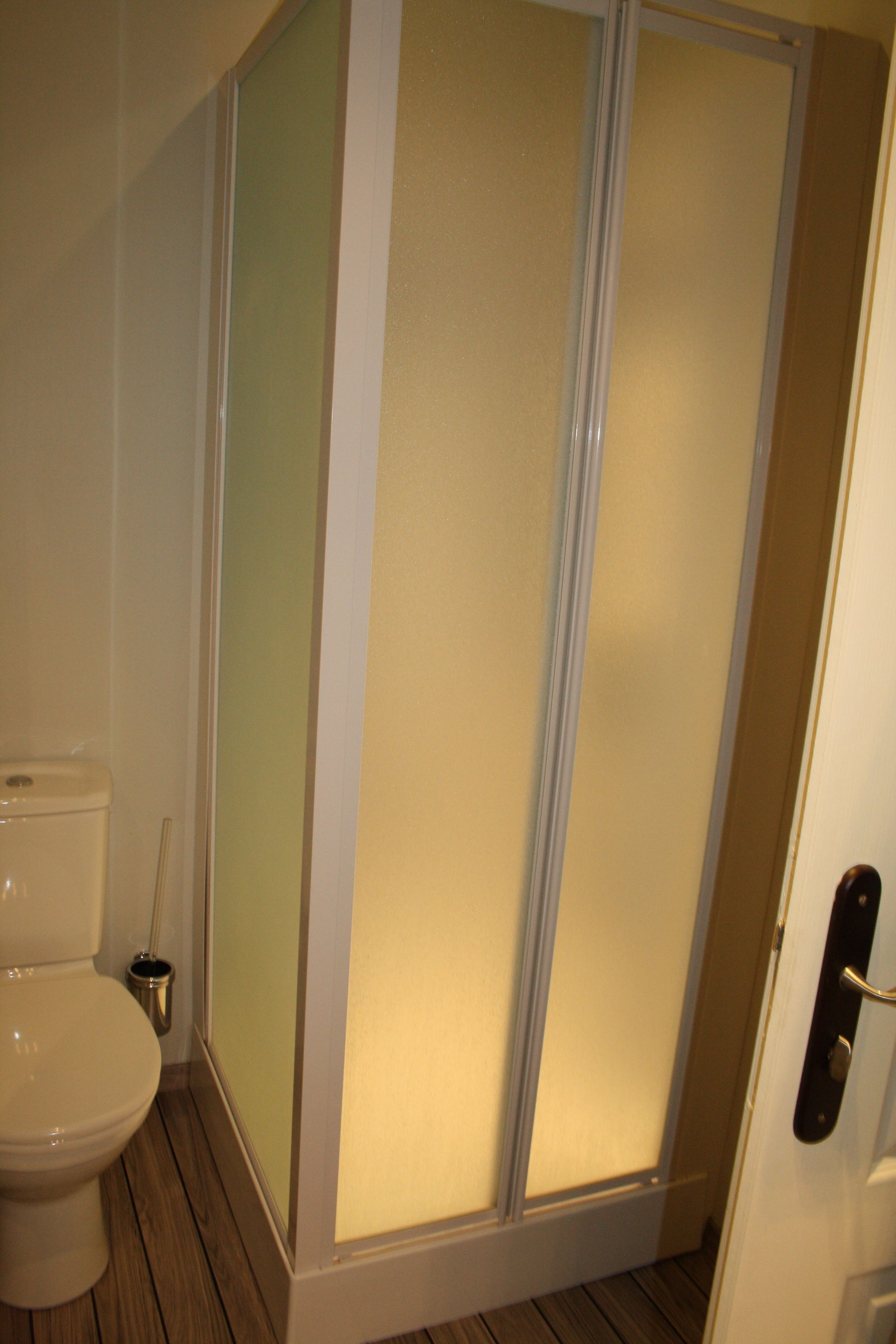A bathroom with a toilet, a shower enclosure, and a door with a handle.