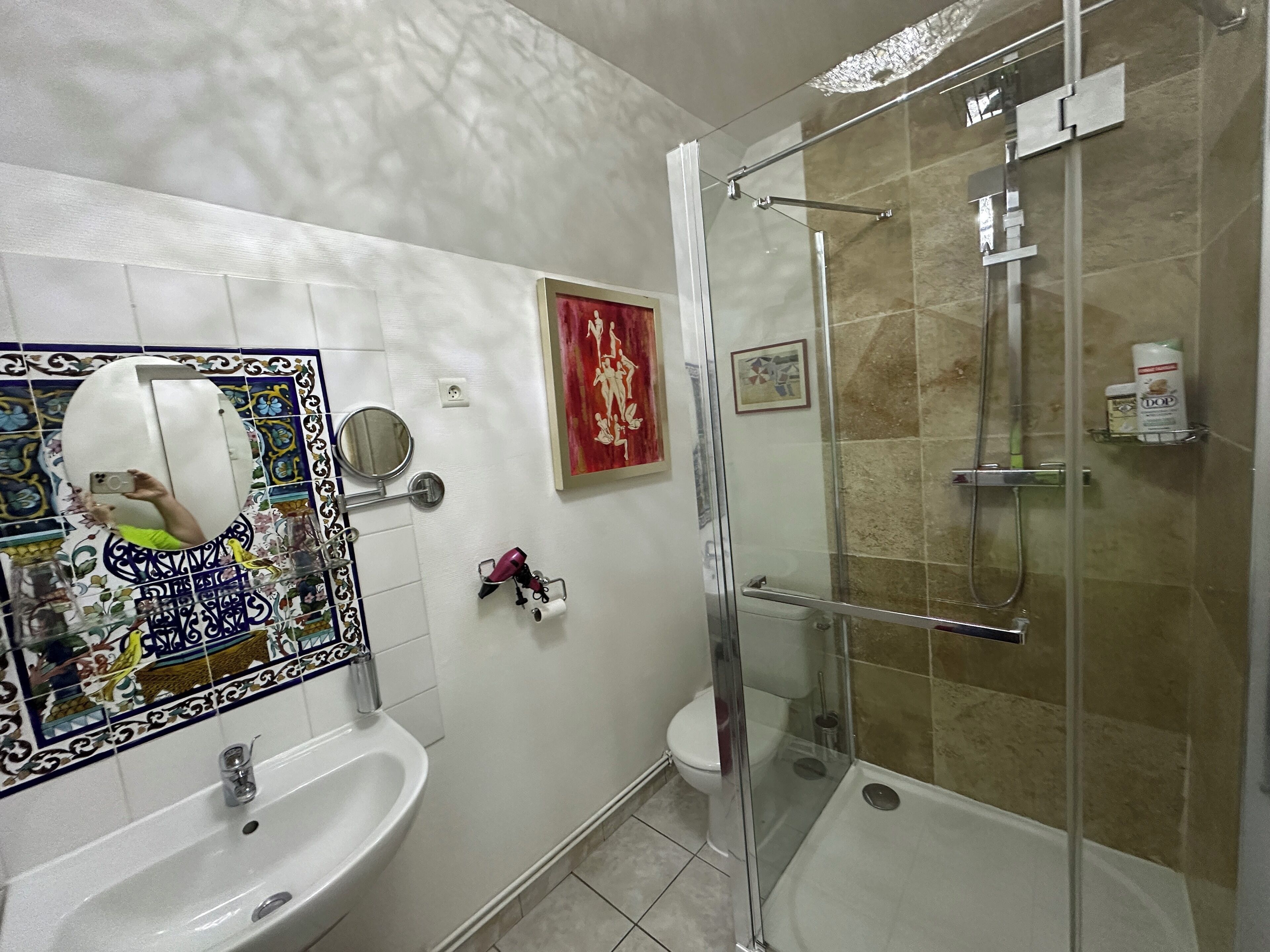 Une salle de bain dotée d’une douche à parois de verre, d’un lavabo, de toilettes et d’un miroir agrémenté d’un pare-éclaboussures décoratif en carreaux.