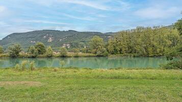Un paisaje sereno con un río, riberas cubiertas de hierba y una colina boscosa al fondo.