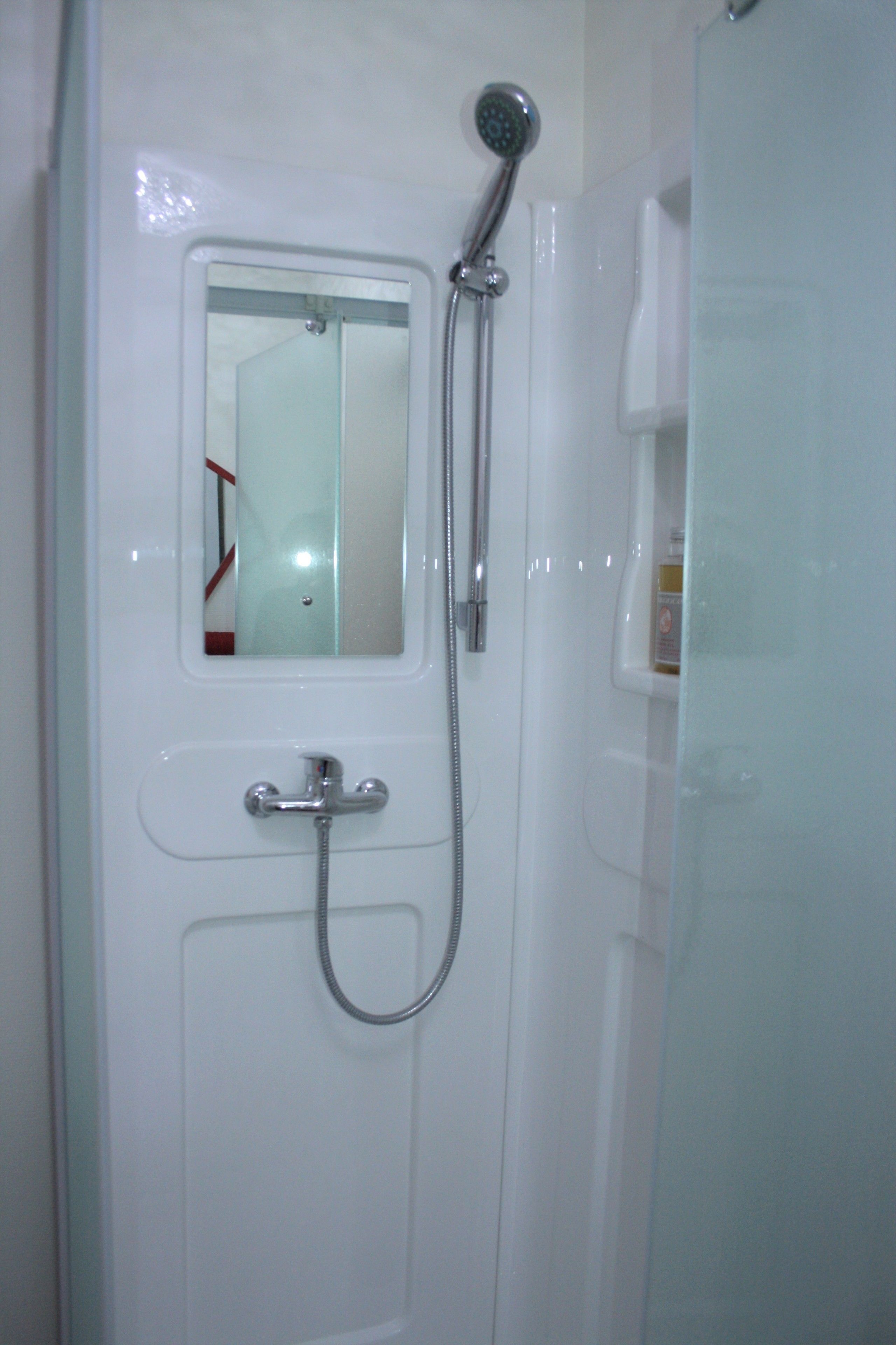 A bathroom with a shower, a mirror, and a soap dispenser.