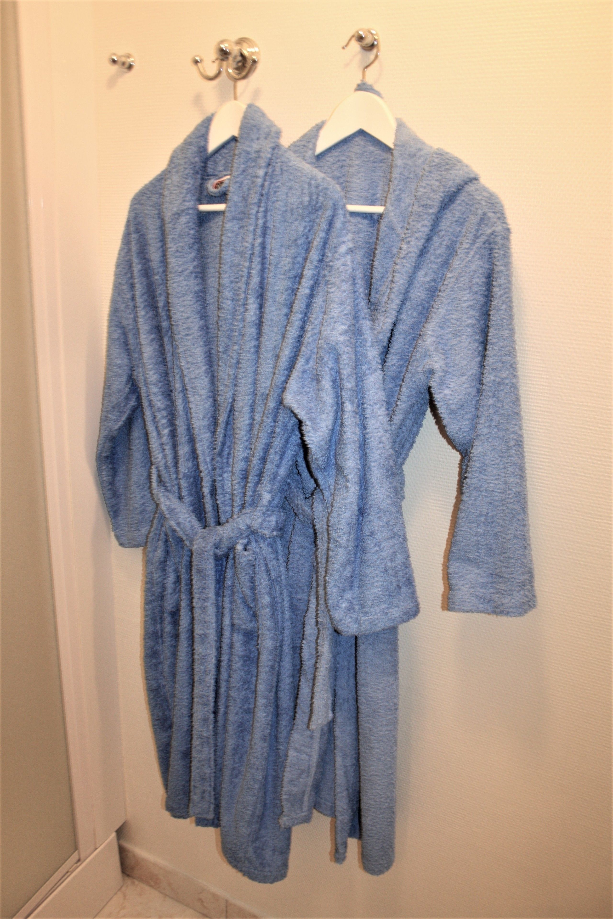 Two blue bathrobes hanging on a door.