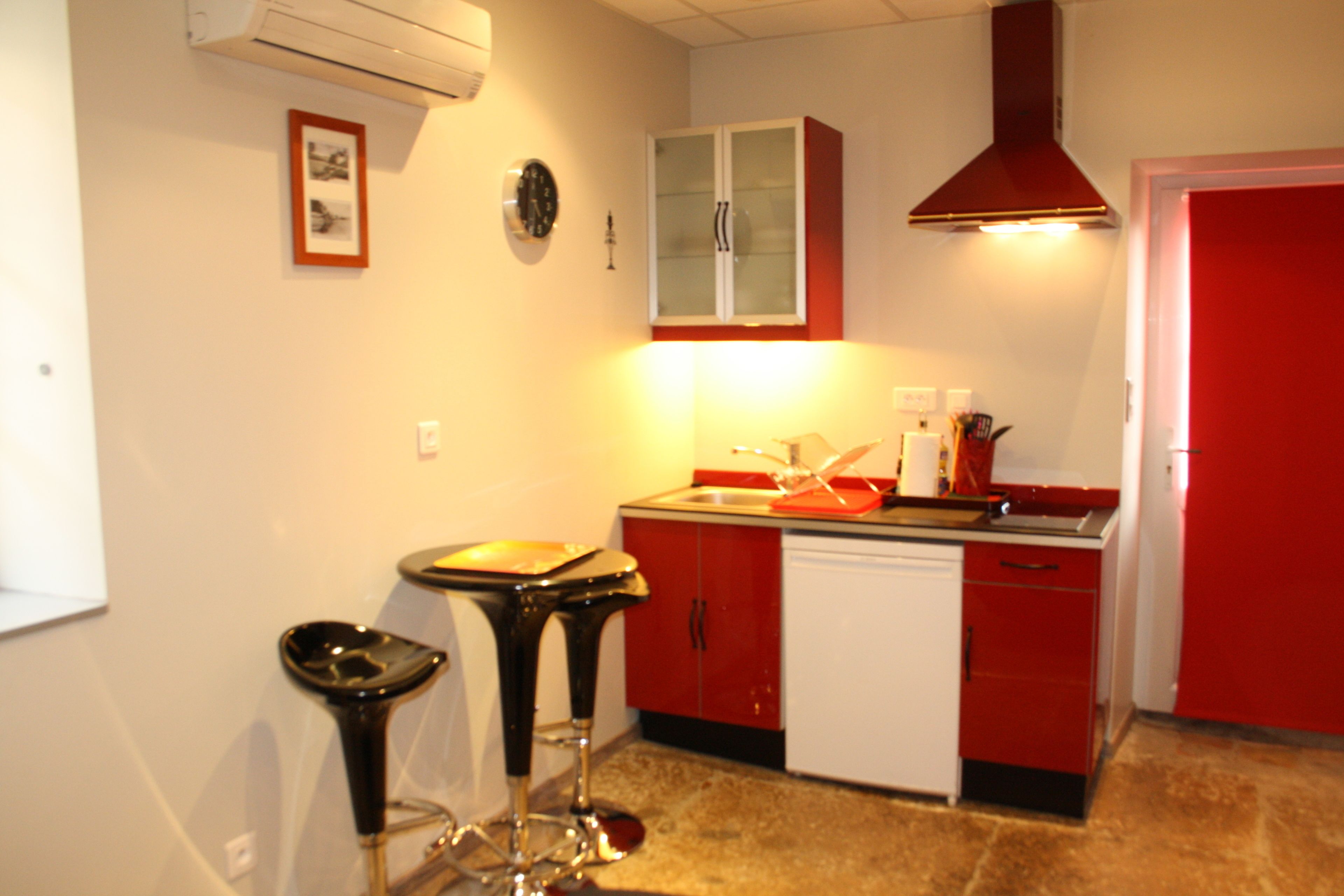 A kitchen with red cabinets, a white dishwasher, and a black bar stool.