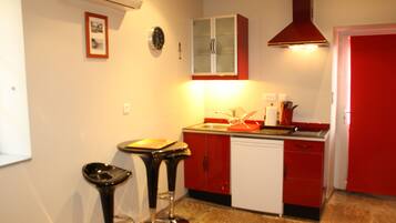 A kitchen with red cabinets, a white dishwasher, and a black bar stool.