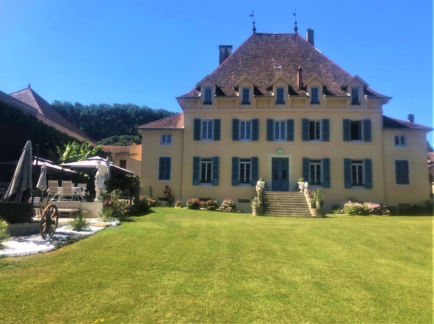 Un grand bâtiment à deux étages, doté d’une façade symétrique, de nombreuses fenêtres avec volets et d’une entrée centrale surmontée d’un escalier.