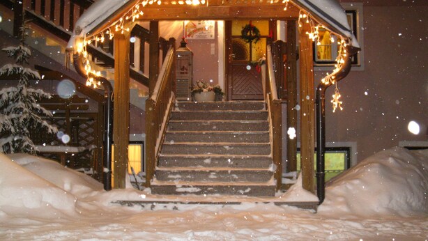A wooden cabin with a staircase leading to a porch, surrounded by snow.