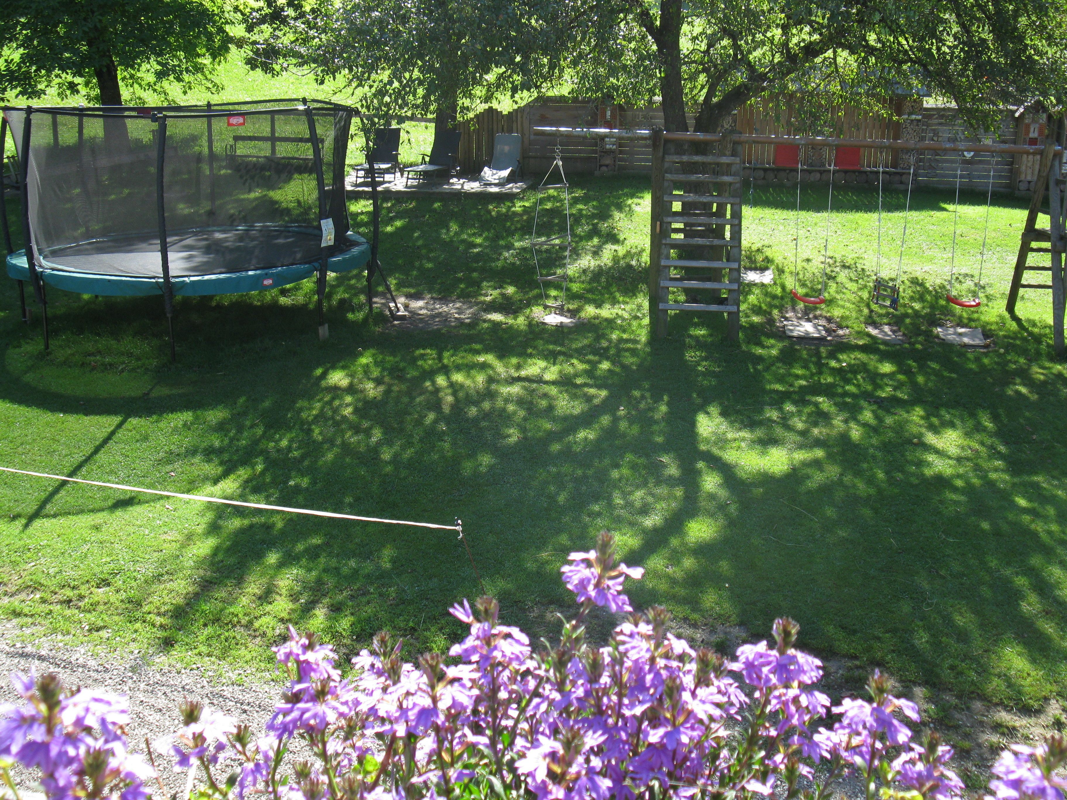 A backyard with a trampoline, swing set, and a wooden ladder.