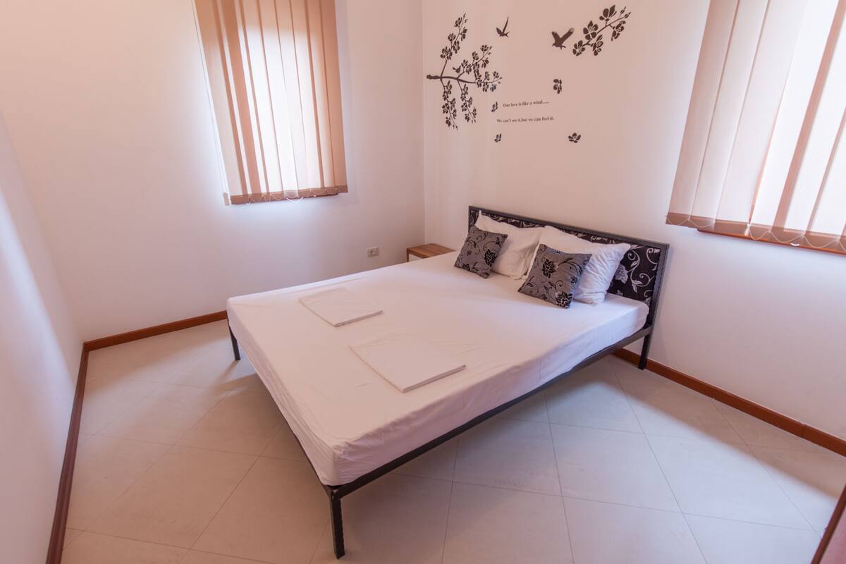 A bedroom with a bed, a nightstand, and a window with blinds.