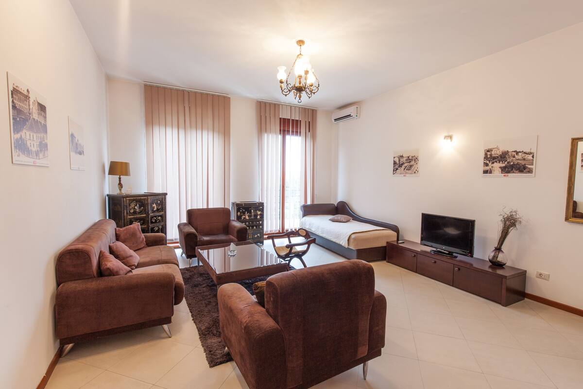 A modern living room with a sofa set, a coffee table, a TV, and a chandelier.