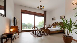 A bedroom with a bed, a wooden chair, a potted plant, a television, and a balcony with a railing. - The Belgrade Hills (Belgrade)