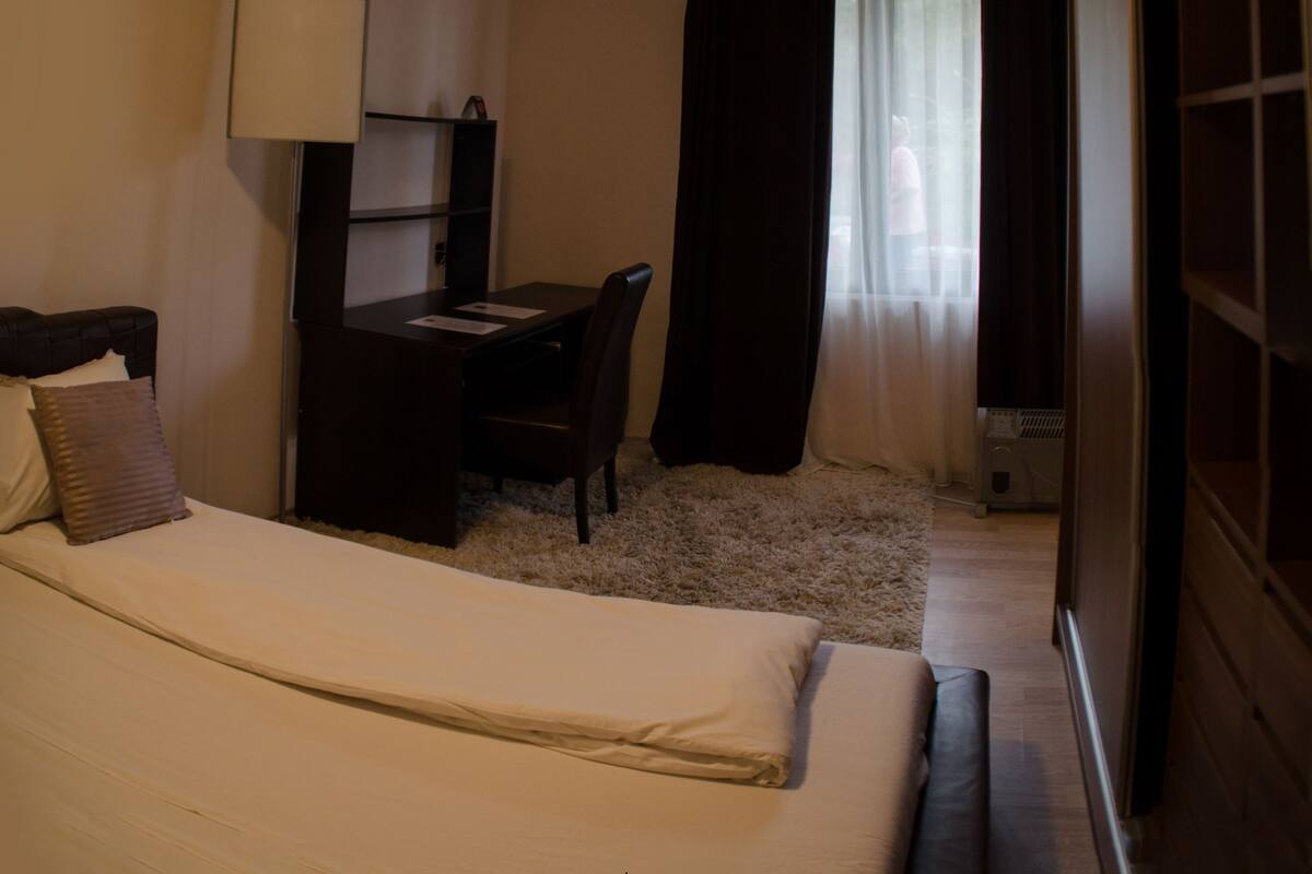 A hotel room with a bed, a desk, a chair, and a window with curtains.