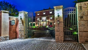 A gated entrance to a building with a brick facade, a paved driveway, and a well-lit entrance area. - The Belgrade Hills (Belgrade)