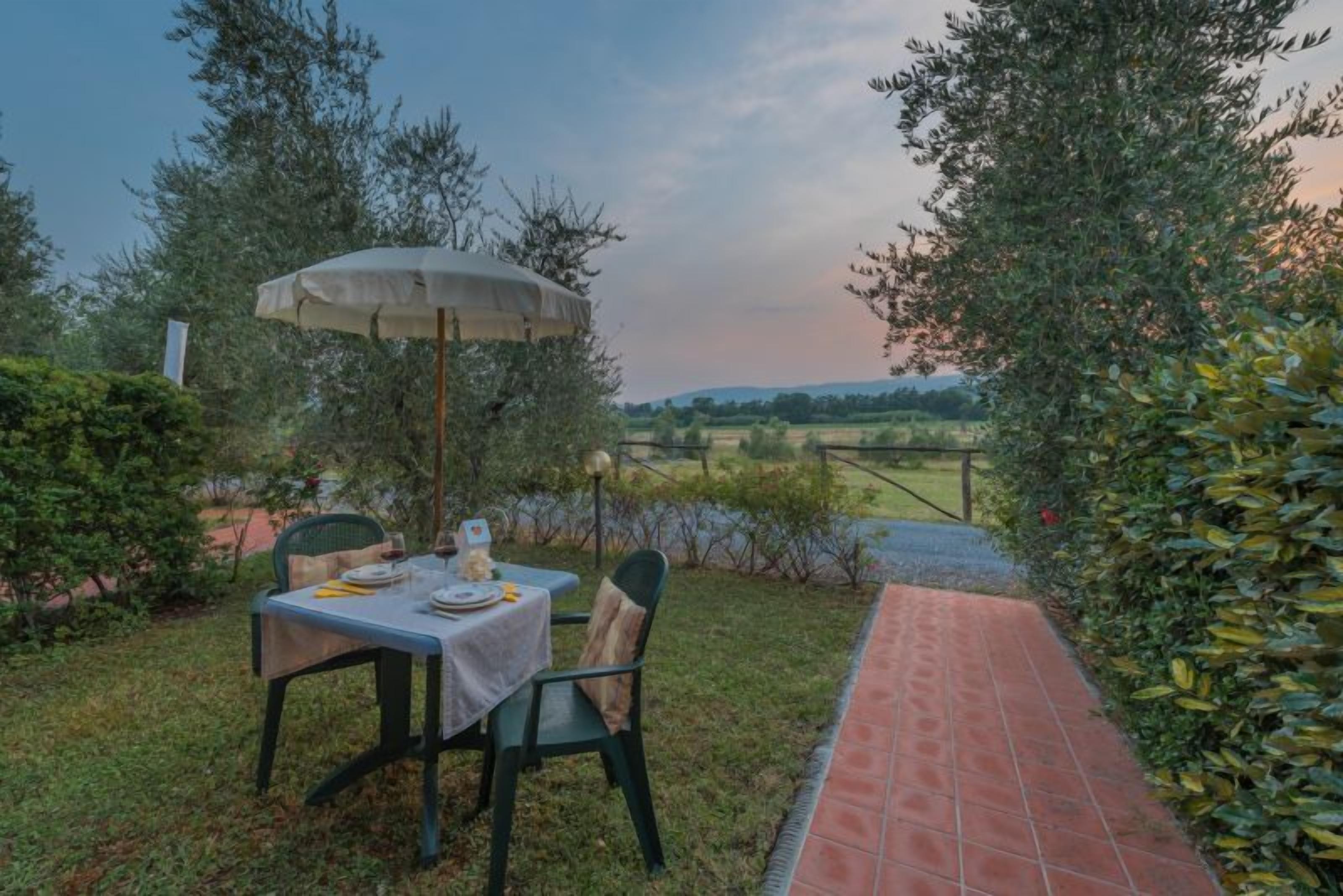 An outdoor dining area with a table set for two, a chair, and a table umbrella.
