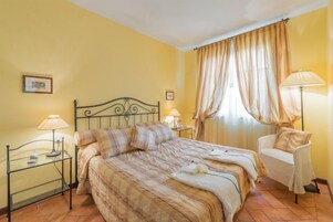 Una habitación de hotel con una cama, dos mesitas de noche, una silla y un ventanal con cortinas.