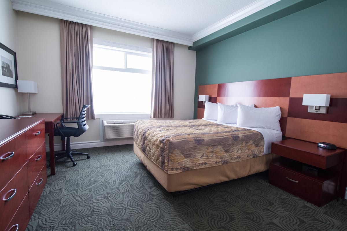 A hotel room with a bed, desk, chair, dresser, and a window with curtains.