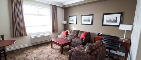 Habitación de hotel con alfombra estampada, dos sofás, una mesita de centro, un escritorio con silla y cuadros en la pared.