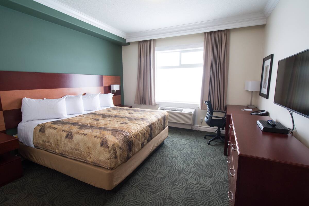 A hotel room with a large bed, a desk with a computer, a chair, and a TV.