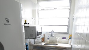 A compact kitchen with a refrigerator, sink, and window. - Leblon Apartment (Rio de Janeiro)